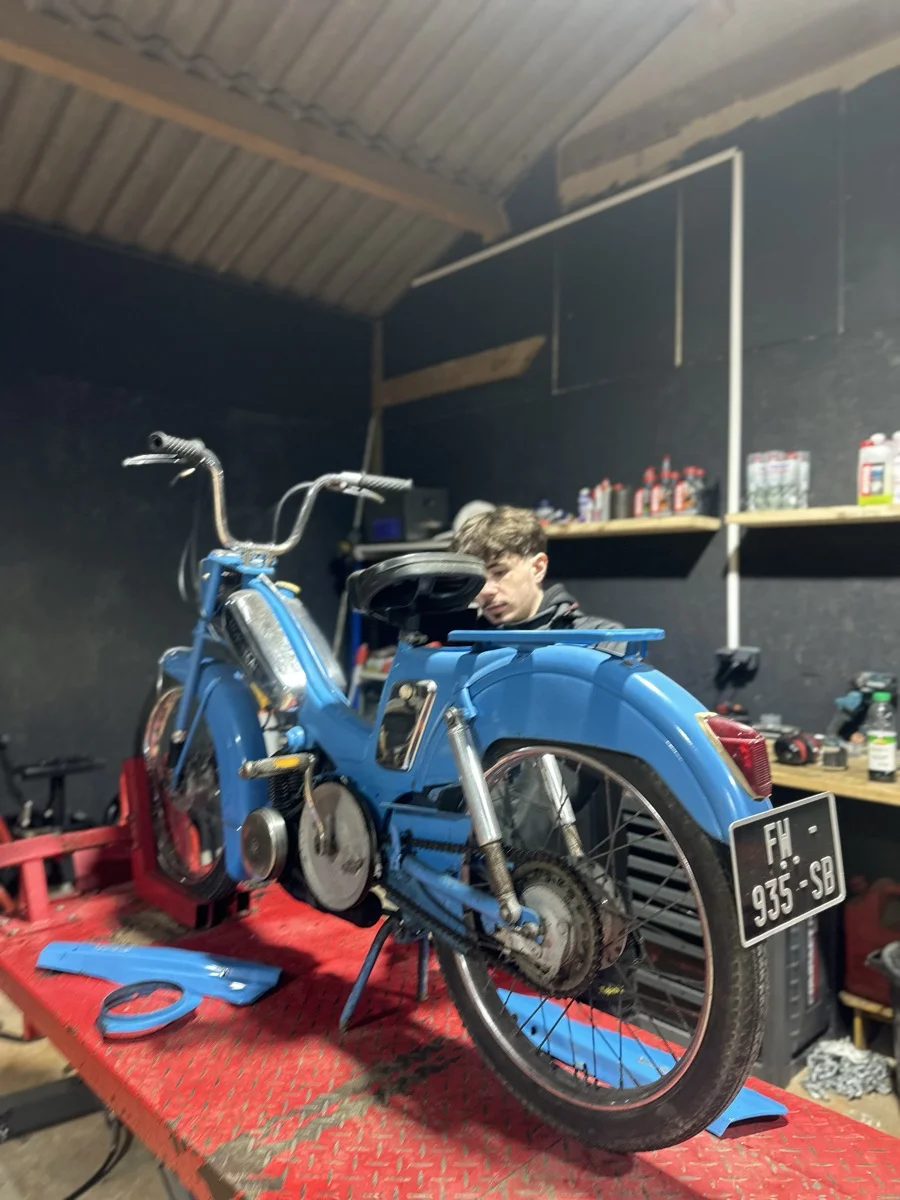 Une mobylette bleue en cours de remise en état sur le pont de l'atelier